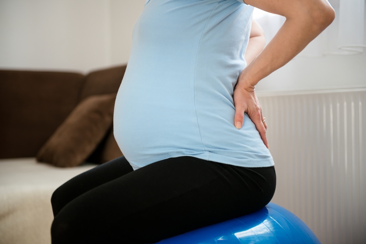 mulher com dor no quadril na gravidez sentada em bola de pilates