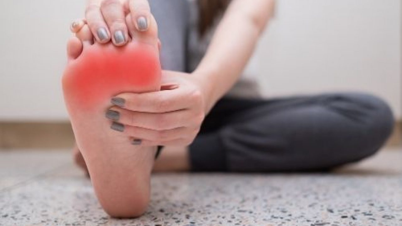 mulher sentada no chão com perna esticada segurando um dos pés com tendinite no pé